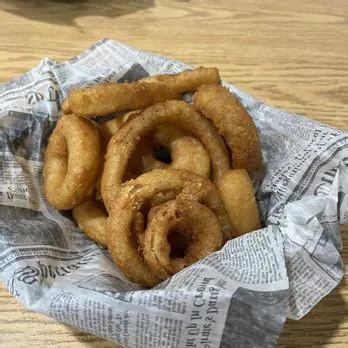 A basket of golden fried onion rings lined with newspaper print paper