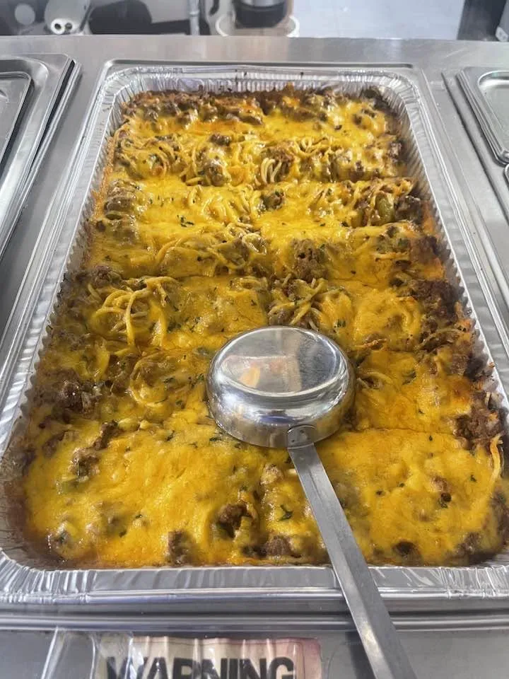 Pans of baked spaghetti with melted cheddar, ladled fresh for a catered event