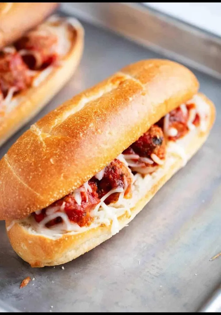 A toasted sub with house marinara and melted cheese on a metal tray