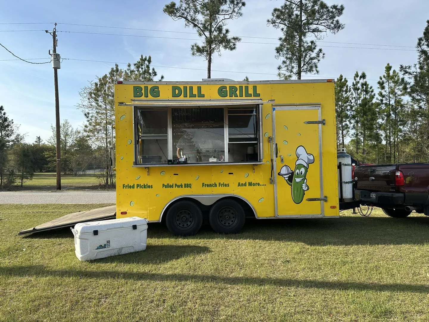 The food truck serving at a grassy outdoor community event with a chalkboard menu in the window